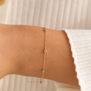 May include: A fine gold chain bracelet featuring three small, round, pale blue gemstones. The bracelet is worn on a wrist. The brand name "HANEL JEWELLERY" is printed at the bottom of the image.