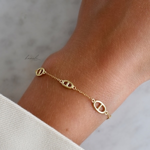 May include: A gold bracelet with a chain link design and oval-shaped charms. The charms have a cutout design resembling a nautical symbol.