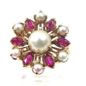 May include: A gold ring featuring a large pearl surrounded by smaller pearls and red ruby stones.