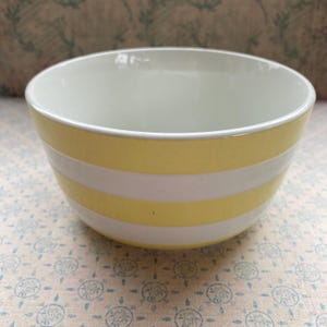 May include: A ceramic bowl featuring a pattern of horizontal yellow and white stripes. The interior of the bowl is solid white, and the exterior displays a repeating design of alternating yellow and white bands around the entire circumference.