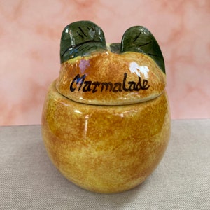 May include: A ceramic marmalade jar shaped like an orange with green leaves on the lid. The jar is decorated with brown and yellow glaze and the word "Marmalade" is written on the lid.