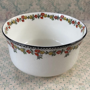 May include: White ceramic bowl with a black rim and a floral pattern of red and yellow flowers. The bowl has a simple, rounded shape and is likely used for serving food or as a decorative piece.