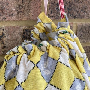 May include: A yellow and grey fabric drawstring bag with a diamond pattern. The bag is gathered at the top and has a white ribbon attached.