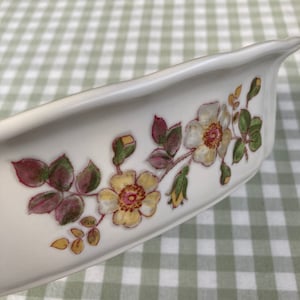 May include: White ceramic oval serving dish with a floral design. The design features yellow, pink, and green roses with leaves.