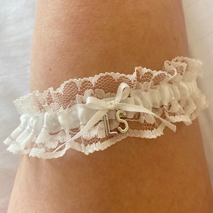 May include: White lace garter with a satin bow and a silver charm with the initials "LS".