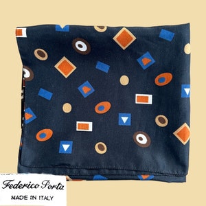 May include: A black silk scarf with a geometric pattern of orange, brown, and blue shapes. The scarf has a label that reads "Federico Porta Made in Italy".