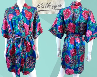 May include: A blue satin robe with a floral print featuring pink roses and green leaves. The robe has a tie belt and short sleeves.