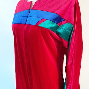 May include: A long-sleeved red velvet jumpsuit with blue, green, and black geometric patterns on the chest and sleeves.