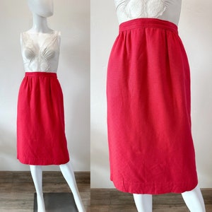 Pode incluir: Uma saia lápis vermelha brilhante com cintura alta e silhueta reta. A saia é feita de um tecido texturizado e tem um design simples.