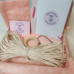 May include: A pink and white polka dot gift box with a white card that says "Southsea Macrame" in purple text. The box contains a ball of natural coloured string, a wooden ring, and a metal hook.