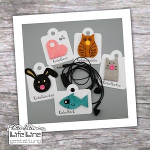 May include: Five different felt cable organizers with various animal designs. The designs include a heart, an owl, a cat, a bunny, and a fish. Each design has a pink nose and the text "Kabelherz", "Kabelwichter", "Kabellotze", "Kabelhäschen", and "Kabelfisch" underneath.
