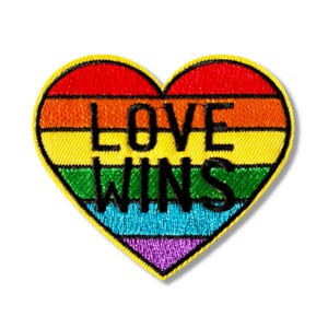 May include: A rainbow heart-shaped patch with the text "LOVE WINS" in black lettering.