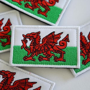 May include: A set of five embroidered patches featuring the Welsh flag. Each patch is white with a green and white stripe across the bottom and a red dragon in the center.