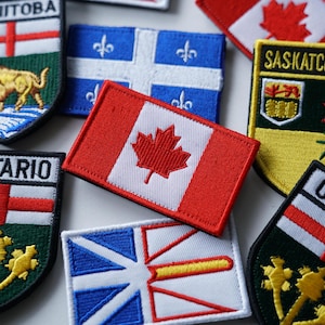 May include: A collection of embroidered patches featuring the Canadian flag and provincial emblems, including Manitoba, Saskatchewan, Ontario, and Quebec. The patches are all in different colours and designs, and they are arranged in a random order.