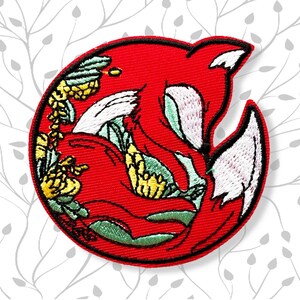 May include: Embroidered patch featuring a stylized red fox curled up in a circle. The fox has white and green accents, with yellow floral details. The patch has a black border.