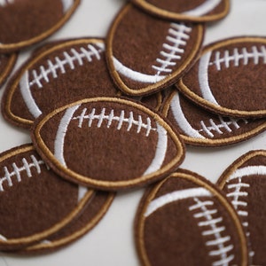 Puede incluir: Un grupo de parches de fútbol de fieltro marrón con costuras blancas. Los parches están dispuestos en una pila, con algunos superpuestos.