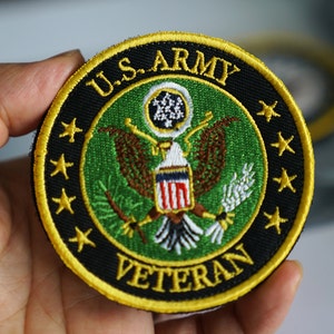 May include: A round, black and gold embroidered patch with the words "U.S. ARMY VETERAN" and a green background featuring the U.S. Army seal.