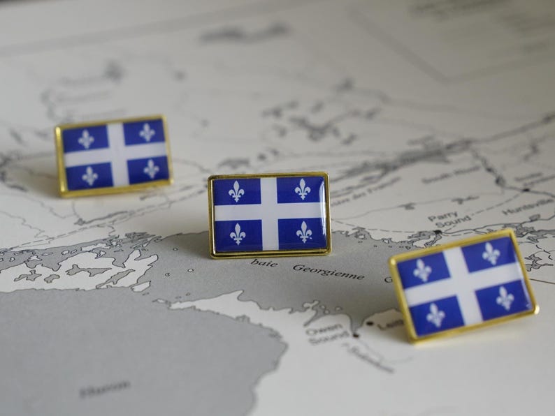 May include: Three gold pins with the flag of Quebec on a map of Canada. The flag is blue with a white cross and four fleur-de-lis.