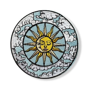 Peut inclure: Écusson brodé avec un motif céleste. Un soleil jaune avec un visage et un croissant de lune sont centrés dans un cercle bleu clair, entouré de nuages blancs. L'écusson a une bordure noire.