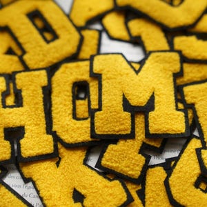 May include: Close-up of yellow felt letters spelling out the word "HOME" with black outlines. The letters are arranged in a random pattern and are slightly overlapping.