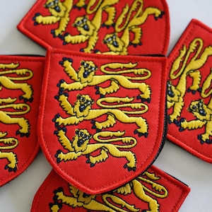 May include: Close-up of several red and gold embroidered patches featuring a heraldic lion design. The patches are shaped like shields and have a black border.