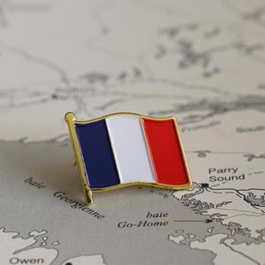 Op de afbeelding: Een gouden emaille pin met de Franse vlag. De vlag is rood, wit en blauw met een gouden rand. De pin is op een kaart met de zichtbare woorden "Parry Sound" en "Go-Home".