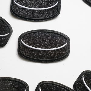 Op de afbeelding: Een set van zes zwarte en witte vilt hockeypuck patches. Elke patch heeft een witte omtrek van een hockeypuck met een zwart midden.