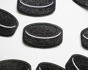 May include: A set of six black and white felt hockey puck patches. Each patch features a white outline of a hockey puck with a black centre.