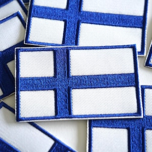 May include: A collection of rectangular patches displaying the Finnish flag. Each patch has a white field with a blue Nordic cross. The blue cross is centrally positioned and reaches the edges. The patches are made of fabric and have a stitched border.