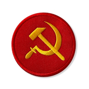 May include: Embroidered patch featuring a yellow hammer and sickle symbol on a red circular background. The patch has a textured appearance, with the design stitched onto the fabric. The hammer and sickle are positioned in the center.