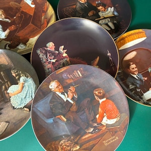 May include: A collection of decorative plates featuring Norman Rockwell illustrations. Each plate showcases a different scene with detailed depictions of people and settings, with gold rims. The plates are arranged on a green surface.