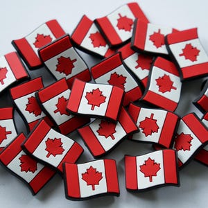 Peut inclure: Un tas de breloques en forme de drapeau canadien rouge et blanc. Les drapeaux sont en caoutchouc et ont un contour noir.