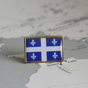 May include: A gold-colored pin with the flag of Quebec. The flag is blue with a white cross and four white fleurs-de-lis.