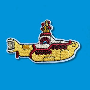 Peut inclure: Patch brodé en forme de sous-marin jaune avec des détails rouges et blancs. Le sous-marin a une fenêtre ronde avec un œil bleu et un périscope avec plusieurs cercles rouges et blancs.