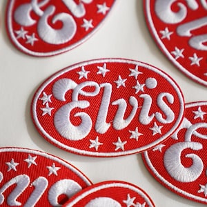 Könnte beinhalten: Rote, ovale gestickte Aufnäher mit weißen Sternen und dem Wort "Elvis" in weißer Kursivschrift.