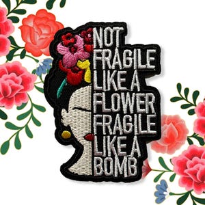 May include: Black embroidered patch with a woman's profile and floral headdress. The white text reads "NOT FRAGILE LIKE A FLOWER FRAGILE LIKE A BOMB." The design incorporates red, pink, and yellow floral details. The patch is a decorative item.