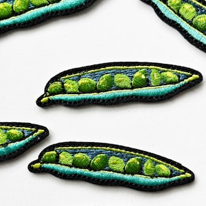 May include: Five embroidered green pea pods with black outlines and turquoise stitching. The pea pods are arranged in a row on a white background.