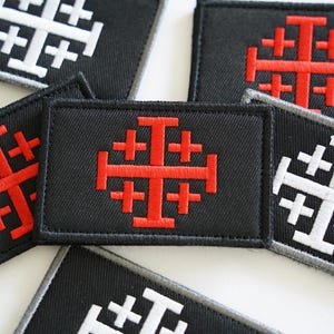 May include: Five embroidered patches featuring a red and white cross design. The patches are made from black fabric and have a white border.