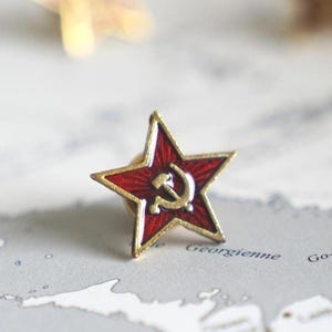 Może przedstawiać: Czerwona gwiazda emaliowana z złotym młotem i sierpem w środku. Gwiazda znajduje się na białym tle z mapą.