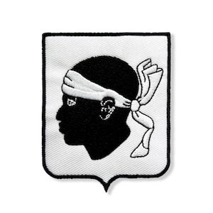 May include: Embroidered patch depicting a black head in profile, wearing a white headband and a white ribbon. The patch is shield-shaped with a white background and a black border. The design is a symbol of Corsica, a French island.