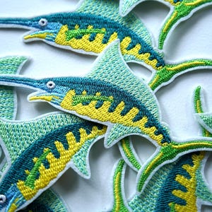 Peut inclure: Écussons brodés représentant un marlin stylisé. Les écussons présentent une palette de couleurs turquoise, jaune et vert, avec des détails de couture complexes. Ils sont probablement destinés aux vêtements ou aux accessoires.