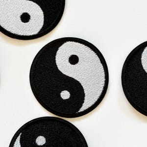 Op de afbeelding: Vier zwarte en witte yin yang geborduurde patches. De patches zijn rond en hebben een witte achtergrond met een zwart yin yang symbool in het midden.