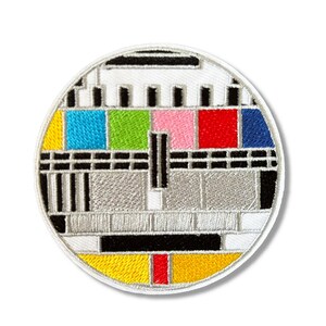 Peut inclure: Un patch rond brodé avec un fond blanc et un motif d'essai de télévision coloré. Le motif comprend des barres noires et blanches, une grille grise et blanche et des carrés colorés en jaune, bleu, vert, rose, rouge et bleu.