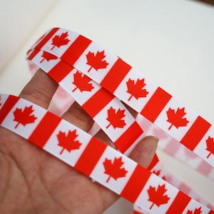 Może przedstawiać: Wstążka z wzorem flagi kanadyjskiej. Wstążka ma naprzemienne czerwone i białe paski, z czerwonym emblematem liścia klonowego na białych paskach. Idealna do rękodzieła i dekoracji.