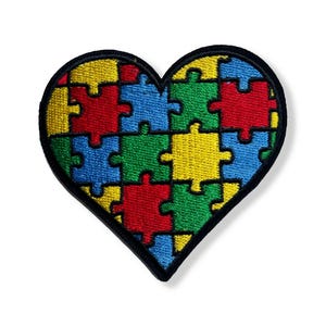 May include: Embroidered heart-shaped patch featuring a puzzle design. The puzzle pieces are in various colors: red, yellow, blue, and green, outlined in black. The patch is designed to be ironed on or sewn onto fabric.