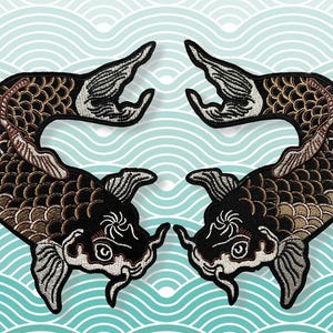 Peut inclure: Deux écussons brodés de carpes koï. Les écussons présentent des motifs détaillés avec des accents noirs, bruns et blancs. Les poissons sont placés sur un fond bleu clair avec un motif de vagues.