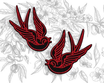 May include: Two embroidered patches featuring a swallow design. The swallows are black with red detailing on the wings and tail. The background is a floral illustration in grayscale.