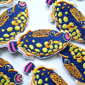 Peut inclure: Écussons de poissons brodés. Les écussons présentent un corps bleu avec des taches jaunes, des accents orange et des détails roses et blancs. Ces écussons sont parfaits pour ajouter une touche unique aux vêtements ou aux accessoires.
