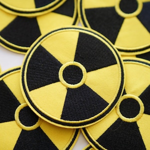May include: A close-up of several yellow and black embroidered patches with a radiation symbol. The patches are round and have a black border.