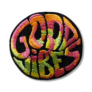 May include: A round, black patch with the words "GOOD VIBES" embroidered in a colourful, tie-dye pattern of pink, orange, yellow, and green.